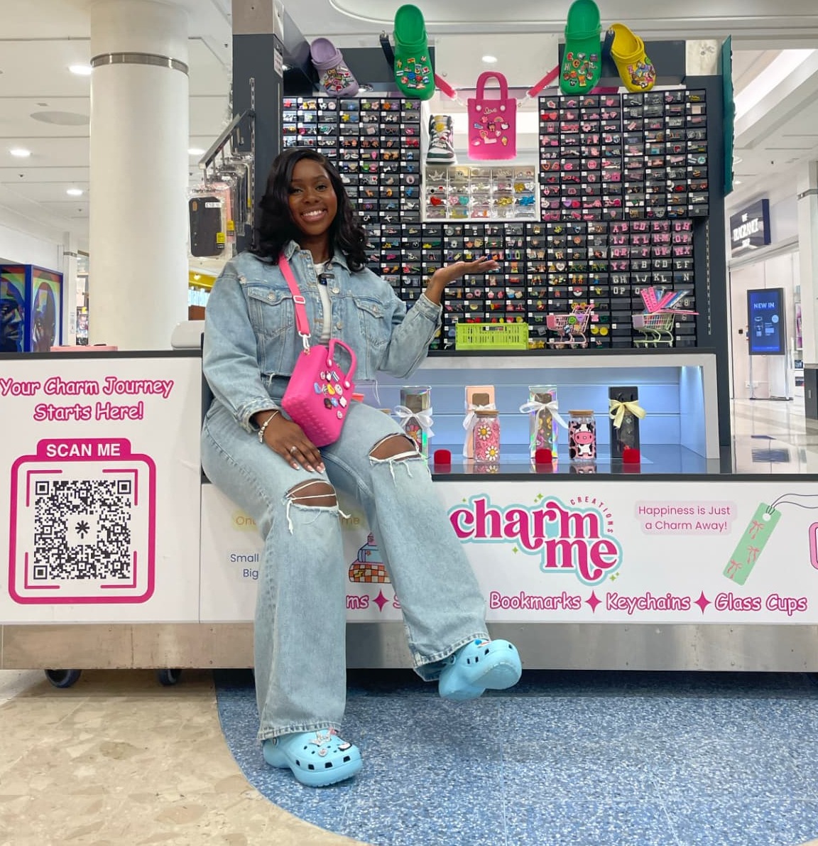 The founder smiling at the counter of her Croydon shopping-centre kiosk, Charm Me Creations, surrounded by colourful charms and handmade products